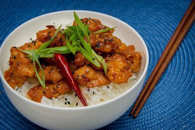 High angle view of fresh meal served in bowl by chopsticks on blue place mat