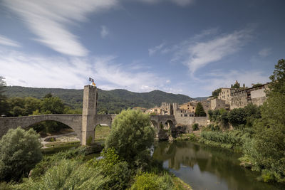 Arch bridge over river by buildings against sky
