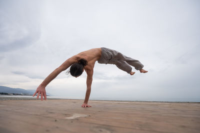 Low section of woman exercising at beach against sky