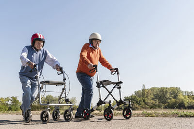 Two old friends wearing safety helmets, competing in a wheeled walker race