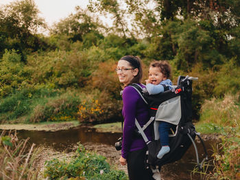 Smiling mother with cute son on back standing on forest