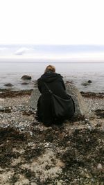 Rear view of woman standing at beach against sky