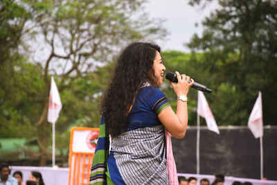 Young woman standing against trees and plants