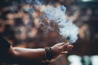 Cropped hand holding lit incense sticks at temple