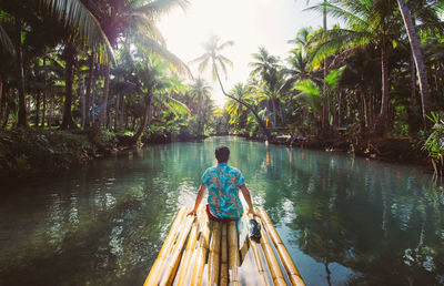 Rear view of man sitting on wooden raft in river