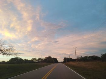 Road by trees against sky during sunset