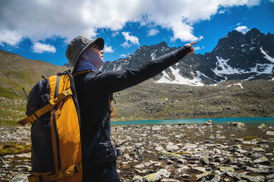 Close up of young caucasian female traveler standing, showing destination mountains, pointing finger
