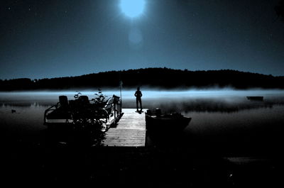 Silhouette men on lake against sky at night