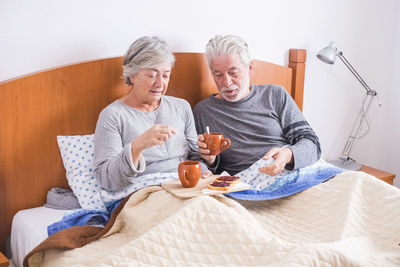 Senior couple eating breakfast on bed at home