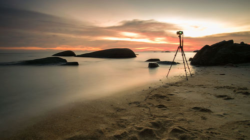 Tripod at beach against sky during sunset