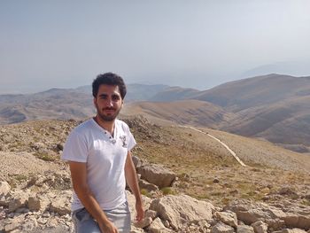 Portrait of young man standing on mountain against clear sky