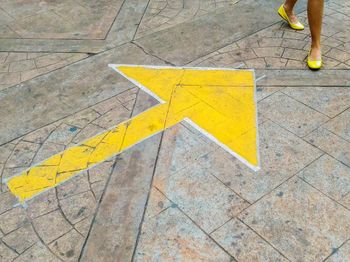 Low section of woman walking by arrow symbol on footpath