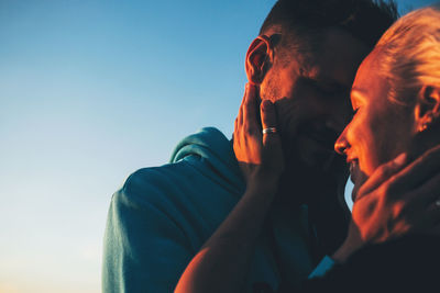 Close-up of couple embracing against blue sky