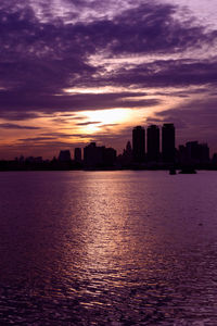 Silhouette buildings by sea against sky during sunset