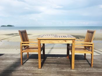 Empty chairs and table on beach against sky