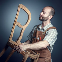 Man holding wooden chair while standing against wall