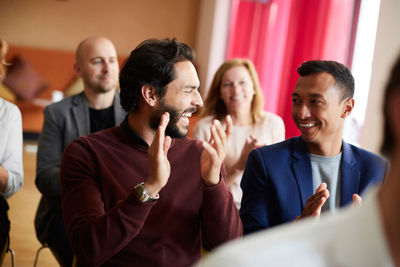 Smiling male and female entrepreneurs clapping while attending office seminar