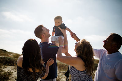 Dad holds baby up as family smiles on beach