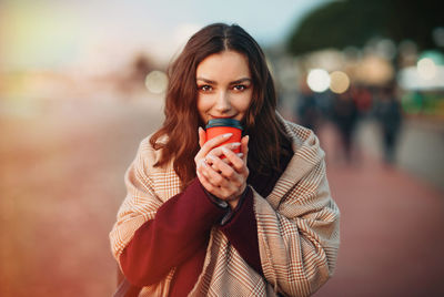 Portrait of young woman drinking coffee while standing outdoors