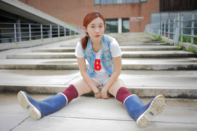 Full length portrait of young woman wearing rubber boots while sitting on steps