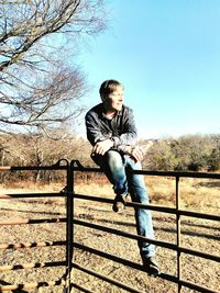 Young man sitting on bare tree against clear sky