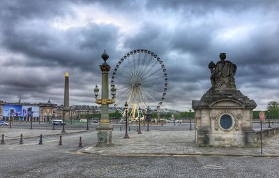 Ferris wheel in city against cloudy sky