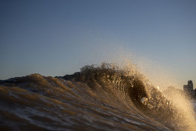 Waves splashing in sea against clear sky