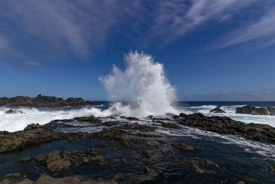 Sea waves splashing on rocks against sky