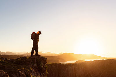 Man standing on rock against sky during sunset