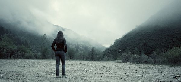 Rear view of woman standing against mountains during foggy weather