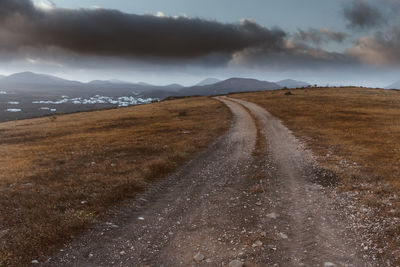 Dirt road leading towards mountains against sky