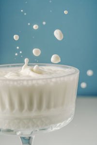 Milk pours into a beautiful crystal glass on a blue background and splashes around.