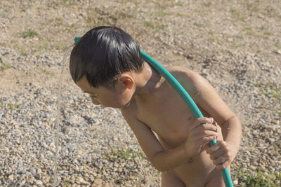 Naked boy playing with water pipe at yard