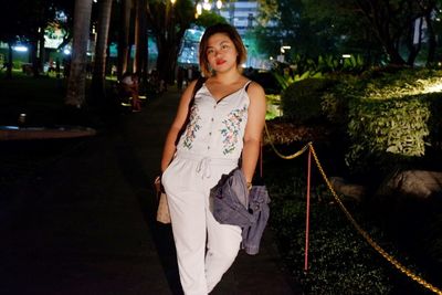 Portrait of young woman standing at park during night