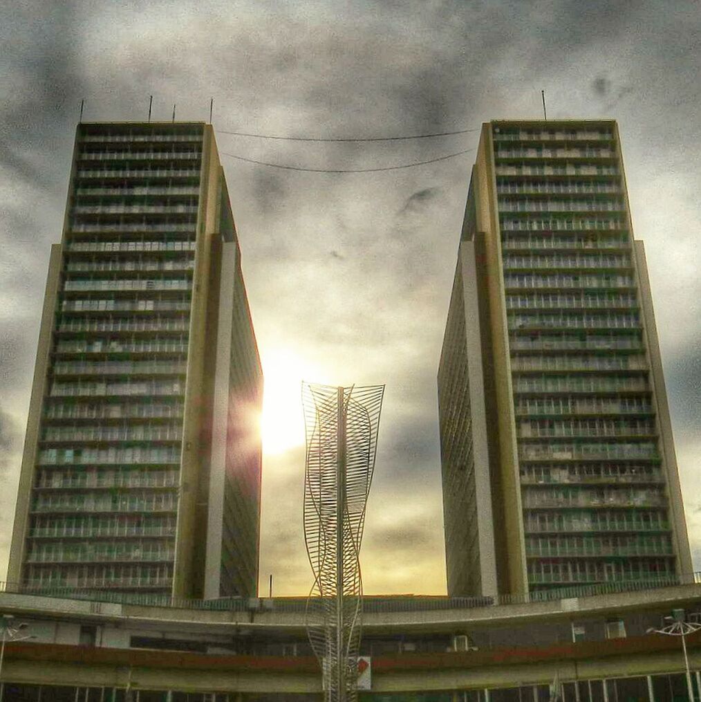 low angle view, architecture, built structure, building exterior, sky, modern, building, cloud - sky, sun, office building, glass - material, silhouette, skyscraper, city, sunlight, tall - high, no people, sunbeam, outdoors, cloudy