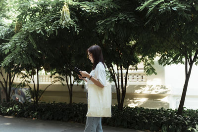 Side view of woman reading book while walking outdoors