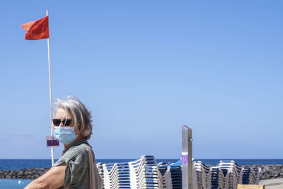 Woman wearing mask at beach against clear blue sky