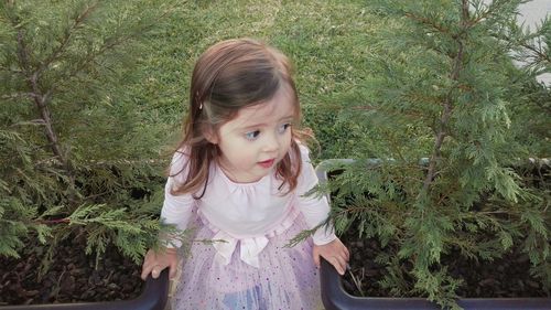 Girl looking away while standing in park by potted plants