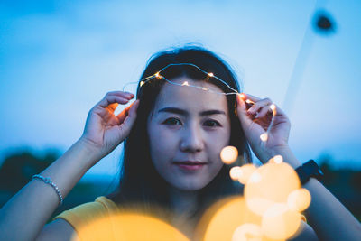 Close-up portrait of smiling beautiful woman holding illuminated string lights