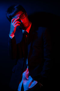 Young man wearing eyeglasses and suit while standing in darkroom