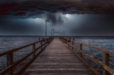 Pier over sea against storm clouds