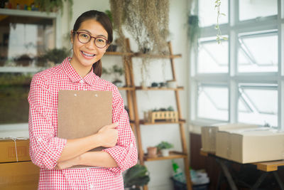 Portrait of smiling businesswoman holding clipboard while standing in office