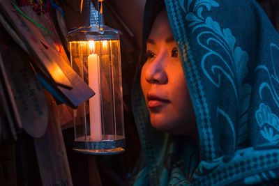 Close-up portrait of young woman holding illuminated lamp