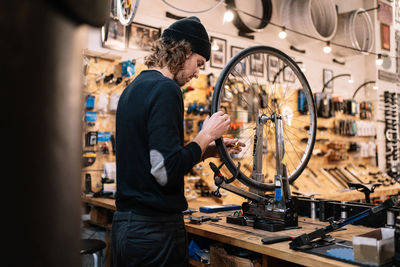 Side view of young male master examining tire on bike wheel while working in professional repair service workshop