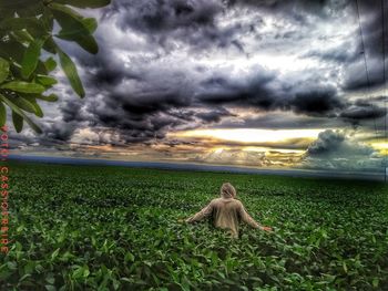 Woman standing on field against dramatic sky during sunset