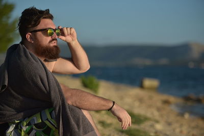 Bearded man sitting at beach against sky