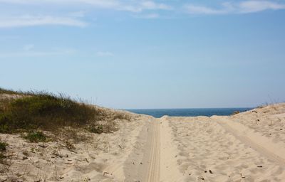 Tire tracks at sandy beach against sky