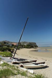 Sailboats moored on beach against clear blue sky