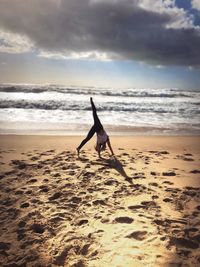 Full length of woman doing handstand at beach against sky