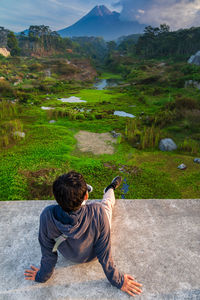 Rear view of man looking at view while sitting on retaining wall